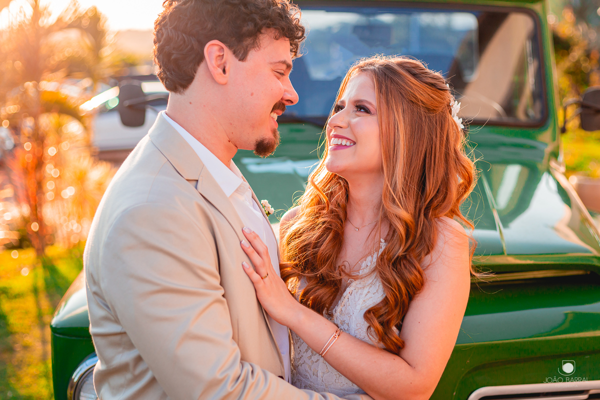 casal de noivos se olhando e rindo com caminhonete verde no fundo