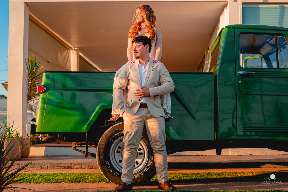 casal de noivos encostado em caminhonete verde olhando para o sol