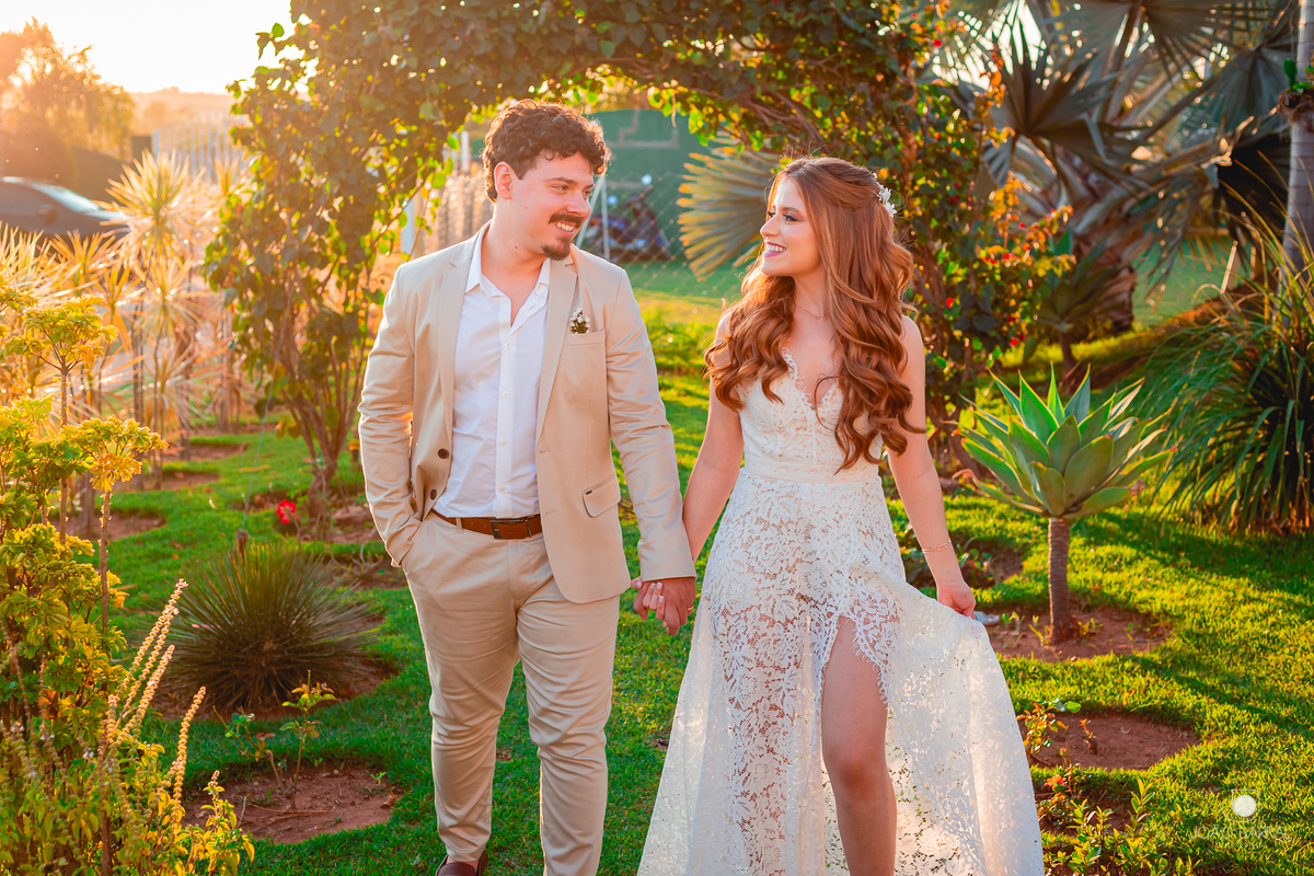casal de noivos andando de mãos dadas em jardim com por do sol