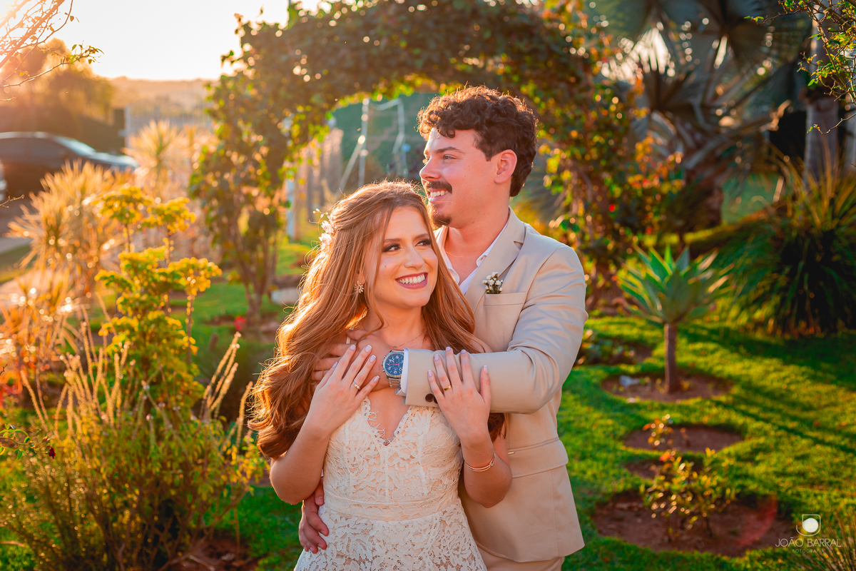 casal de noivos abraçados em jardim com por do sol