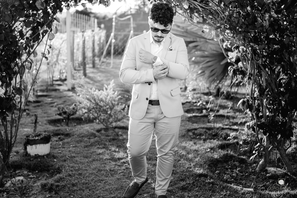 foto preto e branco de noivo de óculos andando e arrumando relógio