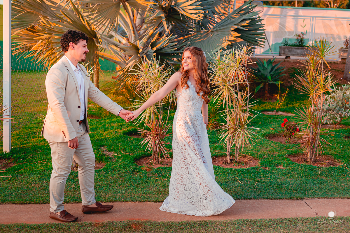 casal de noivos andando de mãos dadas em jardim com por do sol