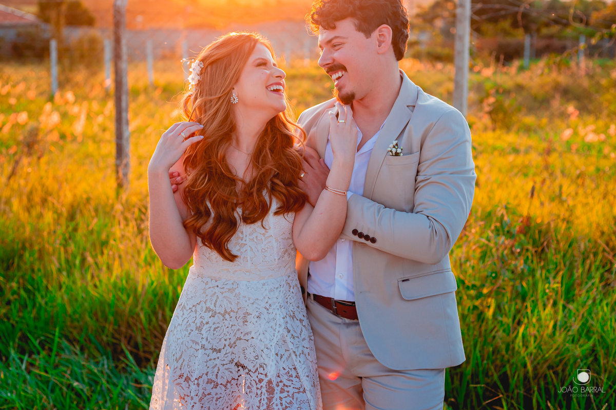 casal de noivos sorrindo e abraçados em jardim com por do sol