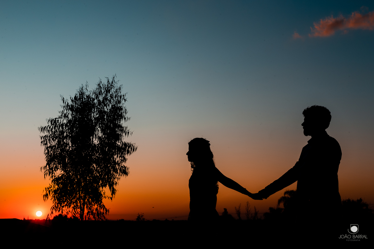 silhueta de casal de noivos andando com o por do sol, céu azul, árvore ao fundo
