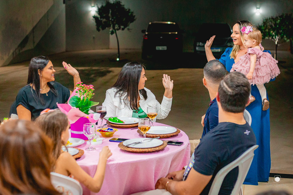 mãe e filha chegando em festa de aniversário e cumprimentando convidados que estão sentados nas mesas