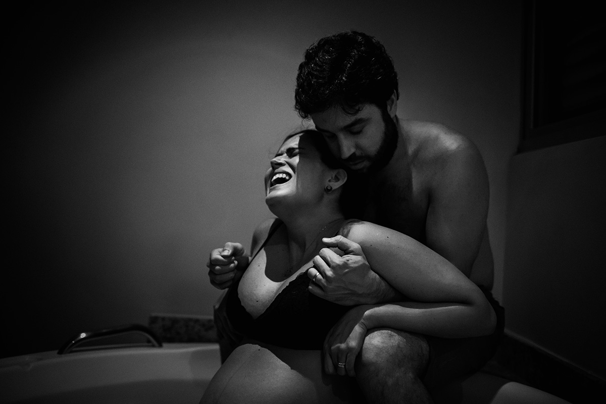 gestante recebe apoio de marido durante contração em um parto humanizado registrado por adrianacostafotos