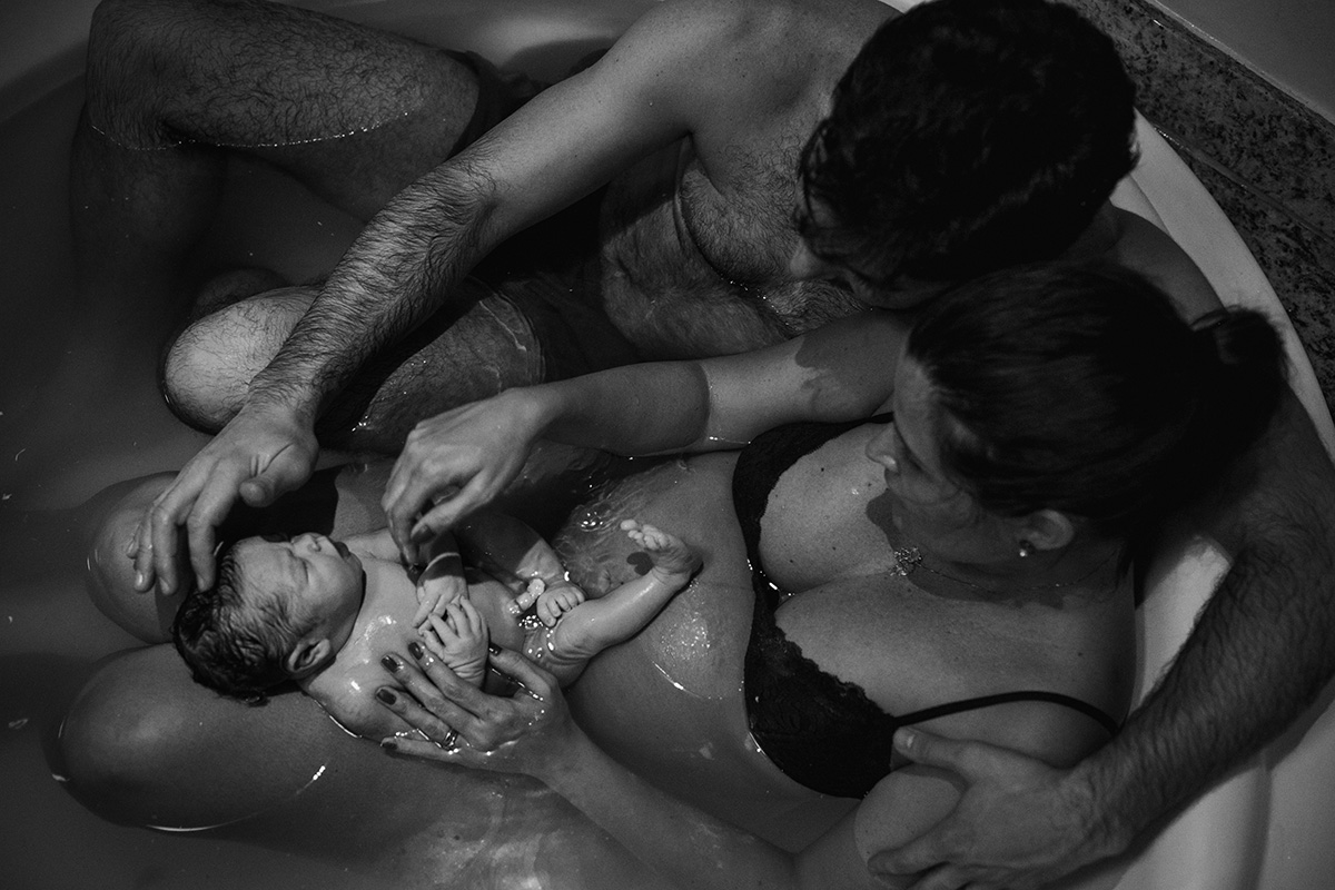 foto de adrianacostafotos da mãe e do pai na banheira descansando com o bebê que acaba de nascer na água