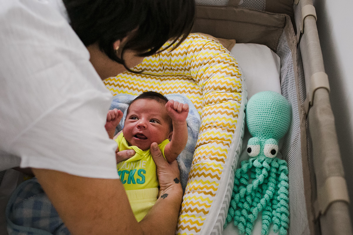 mãe tirando bebê do berço para amamentar em um registro feito por Adriana Costa