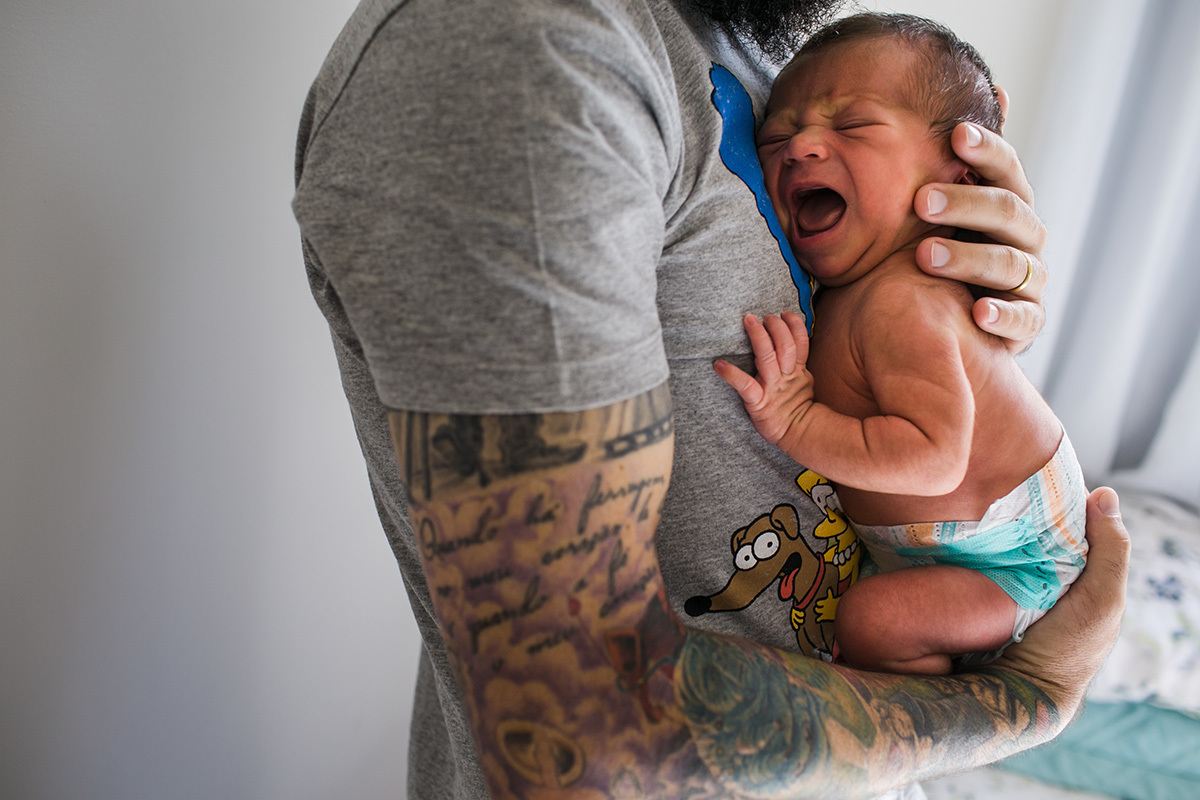 bebê chorando no colo do pai em uma fotografia feita por Adriana Costa