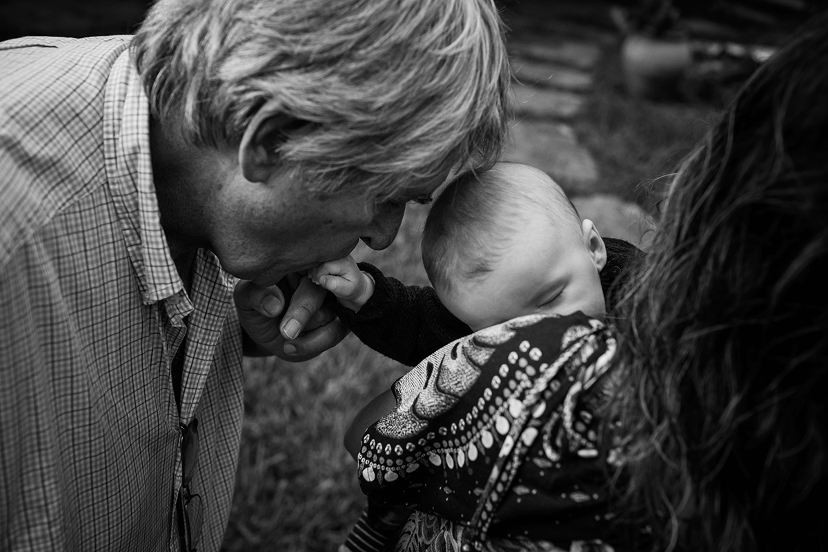 avó beijando a mão do neto que dorme no colo da mãe, por Adriana Costa