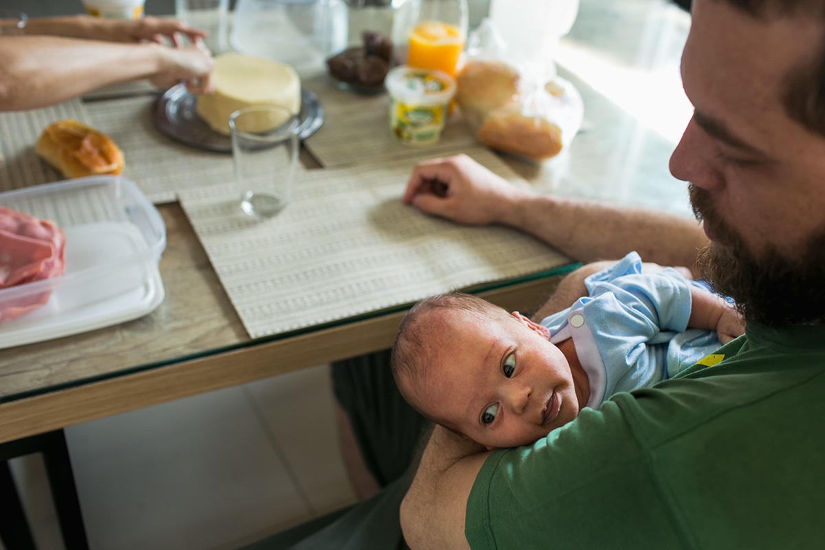 Foto de Adriana Costa do pai tomando café da manhã com seu filho no colo
