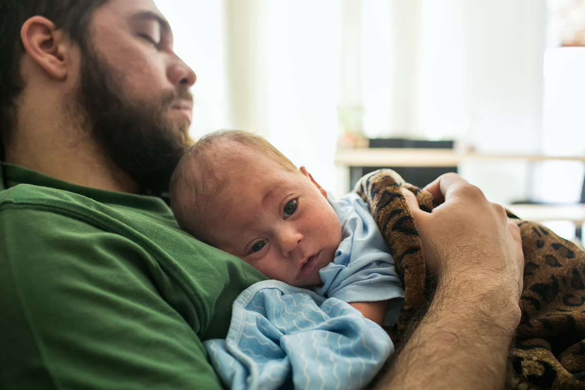 pai dormindo com seu bebê no colo ainda acordado, por Adriana Cossta