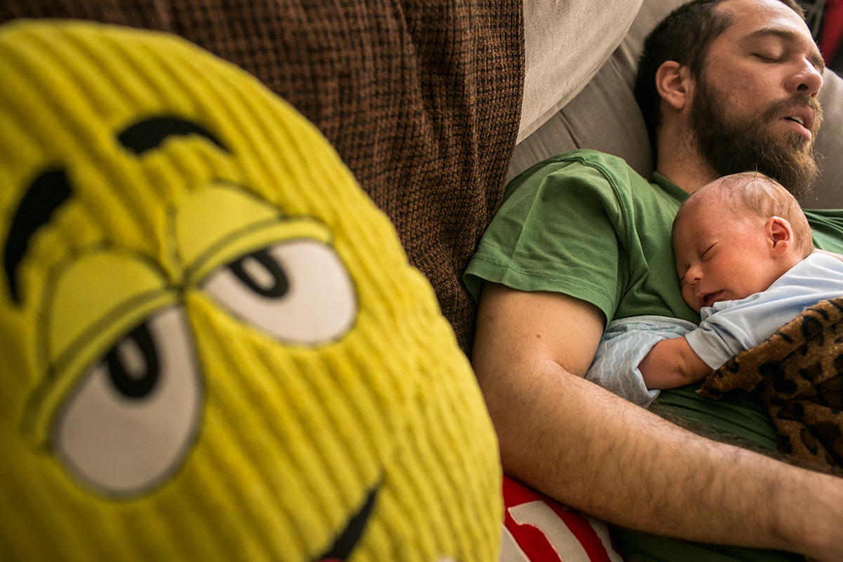 pai e filho dormindo juntos com uma almofada da M&M os observando, em foto cômica de Adriana Costa