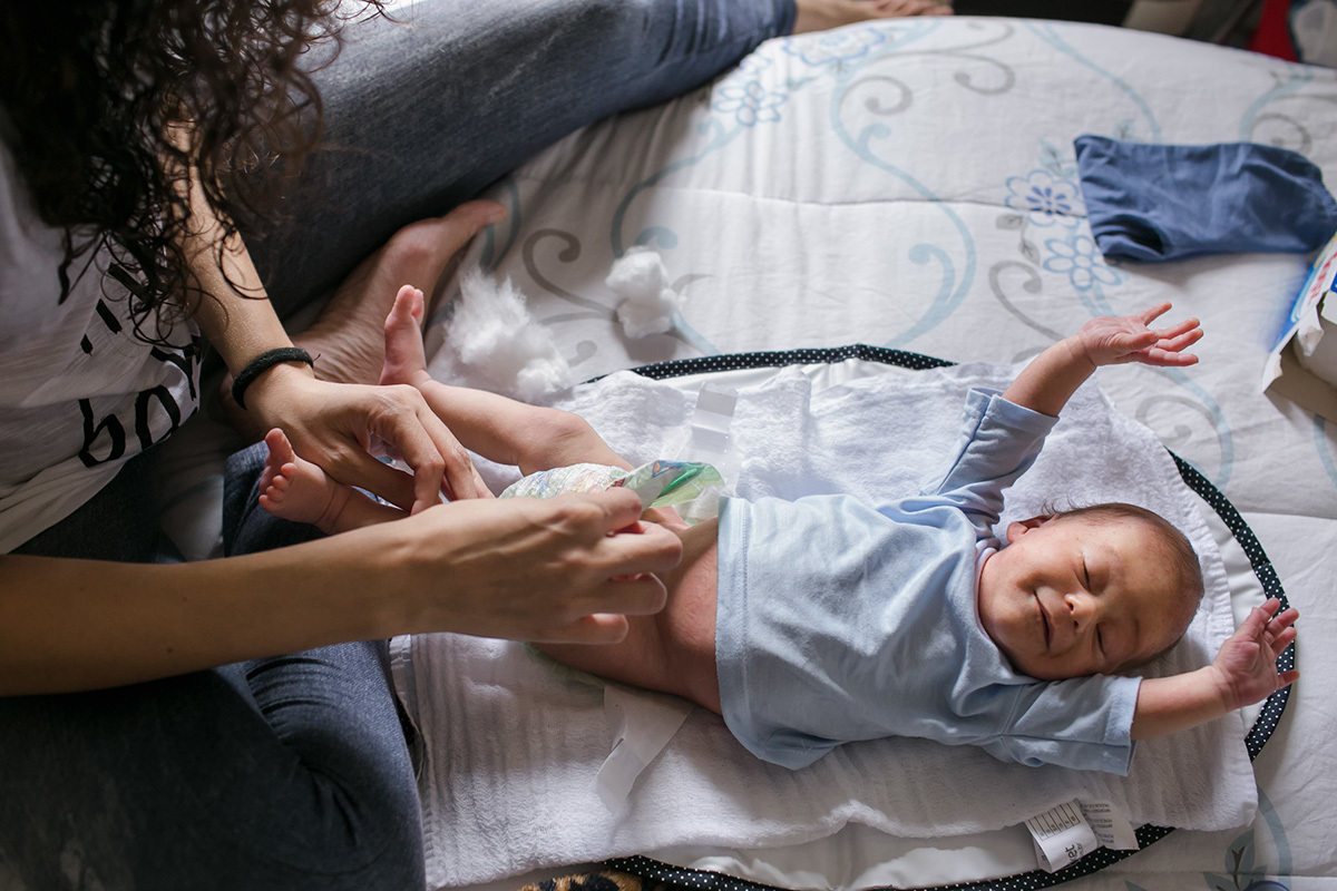 Bebê espreguiçando enquanto a mãe troca sua roupa em foto de Adriana Costa