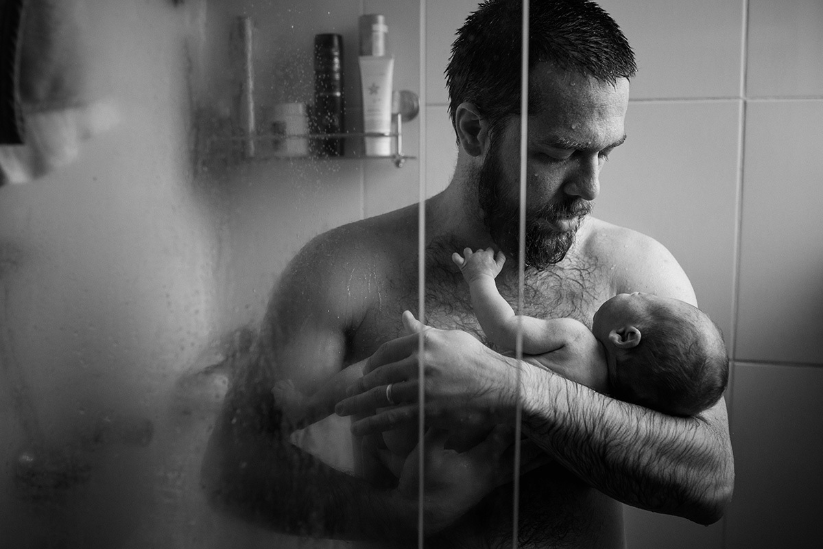 pai dando banho no seu bebê no chuveiro, em uma foto feita por Adriana Costa