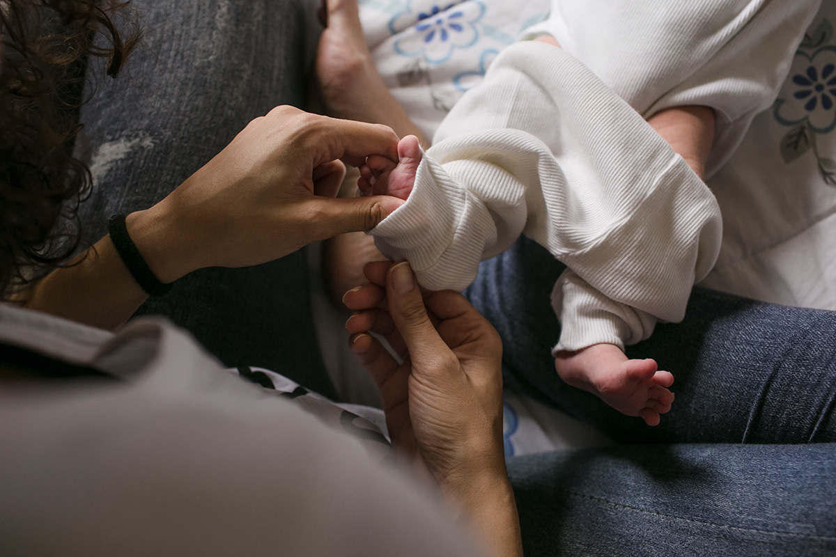mãe colocando a calça no pezinho minusculo do seu bebê, em foto de Adriana Costa