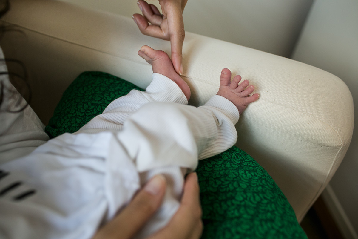 mãe fazendo carinho no pé do seu bebê enquanto ele amamenta, por adrianacostafotos