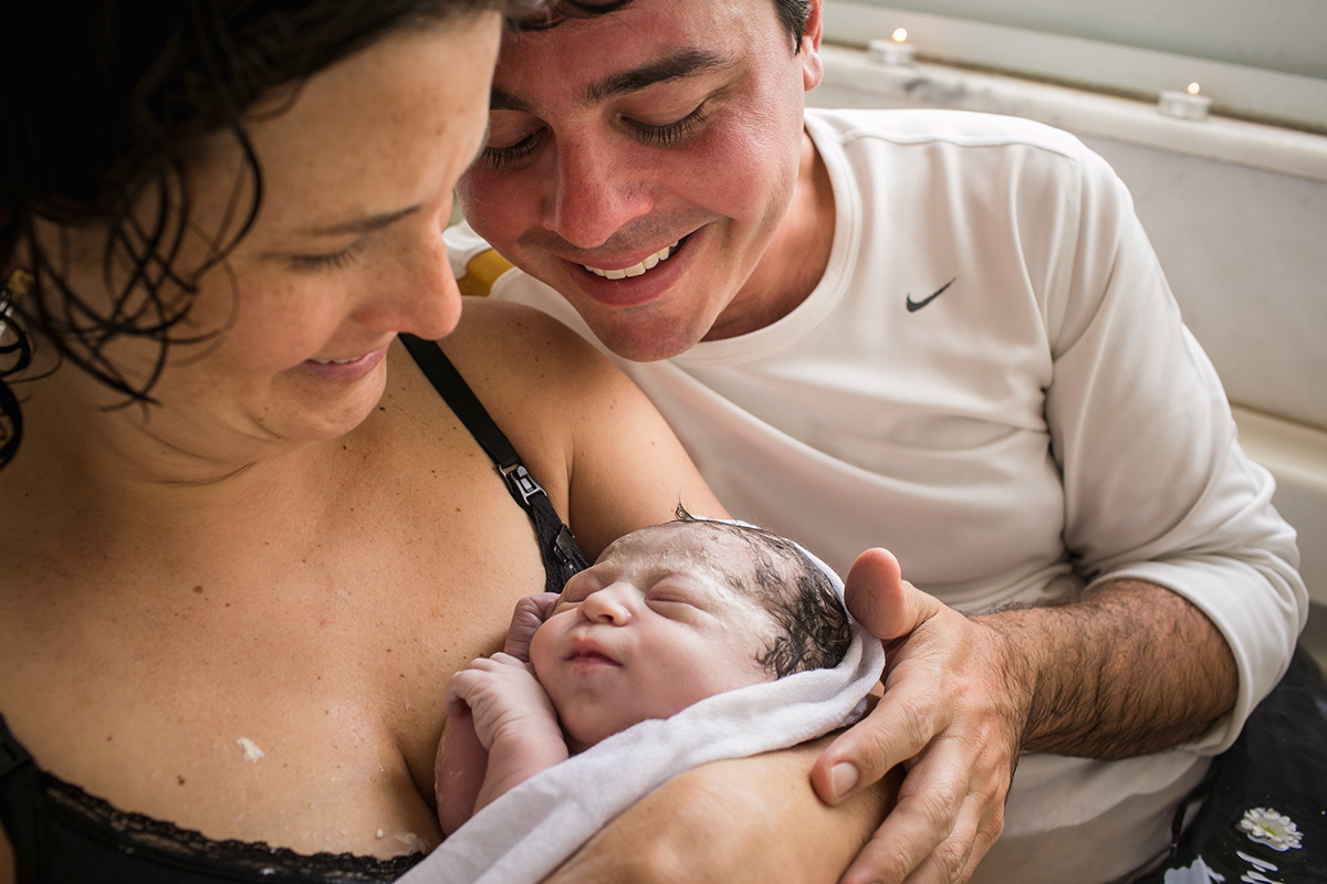 pais sorrindo vendo sua filha após o nascimento