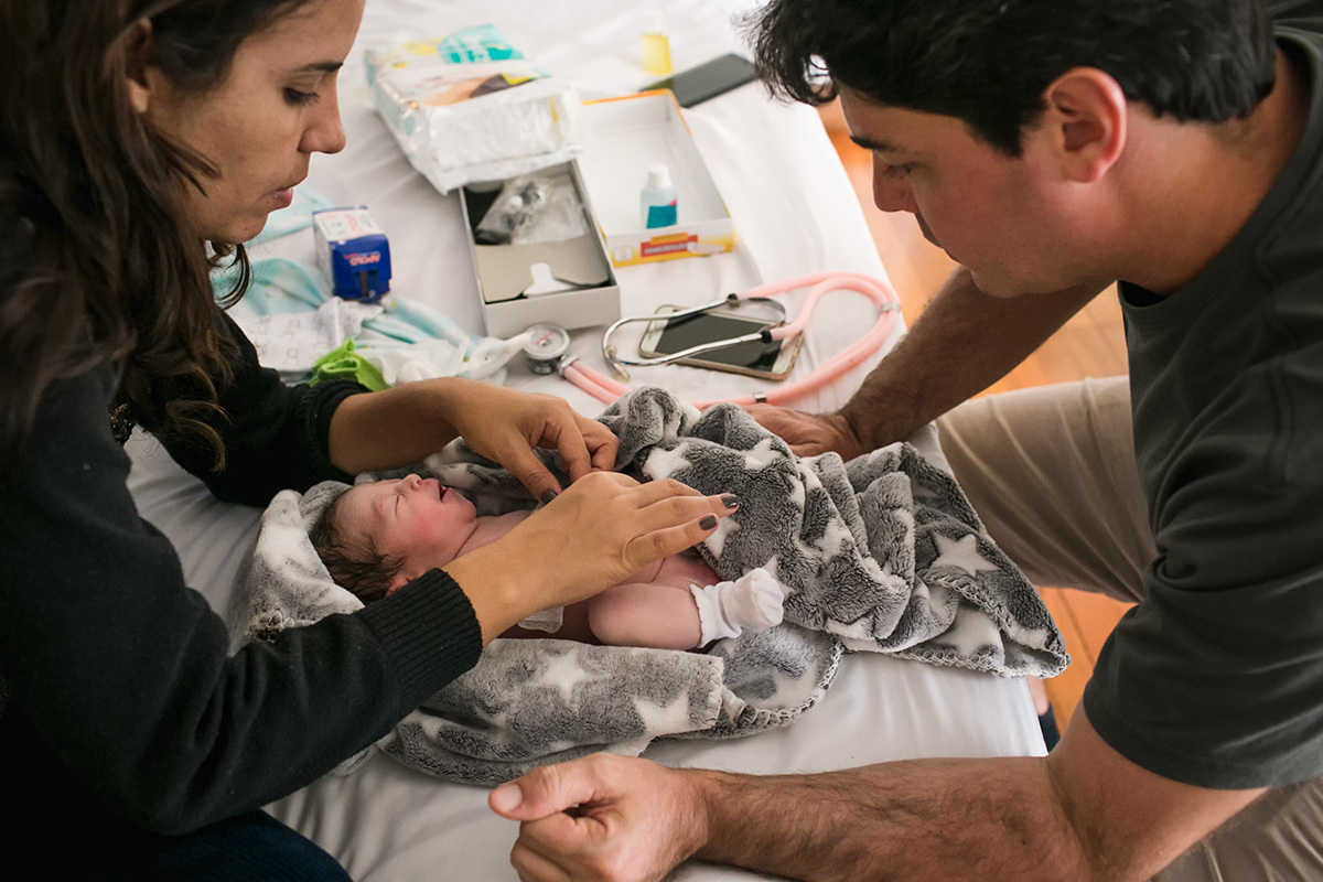 pai observando a enfermeira prestar os primeiros cuidados a sua filha que acabou de nascer, por adrianacostafotos