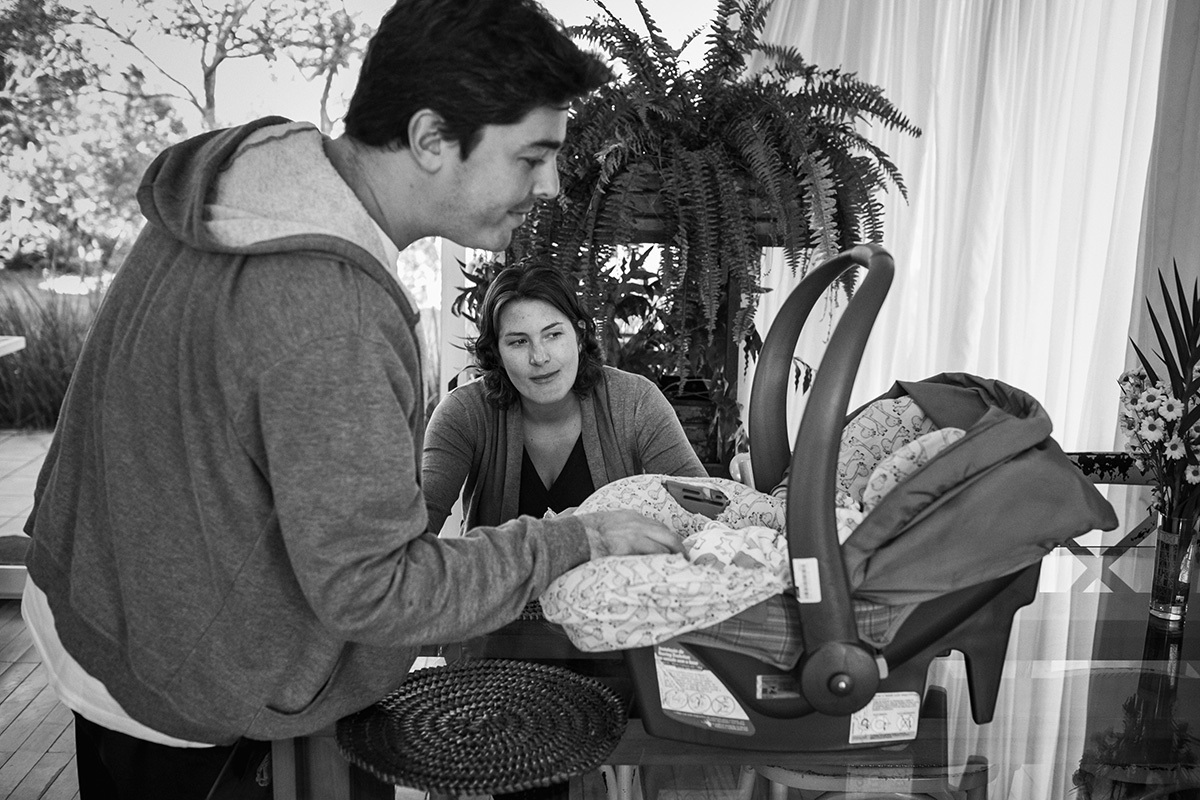 Pai vendo a filha dormindo no bebê conforto que encontra sobre a mesa do café da manhã, por adrianacostafotos