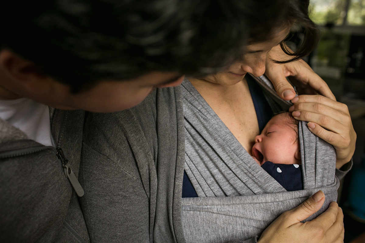 pai e mãe vendo a filha que está no sling wrap bocejar em foto de Adriana Costa