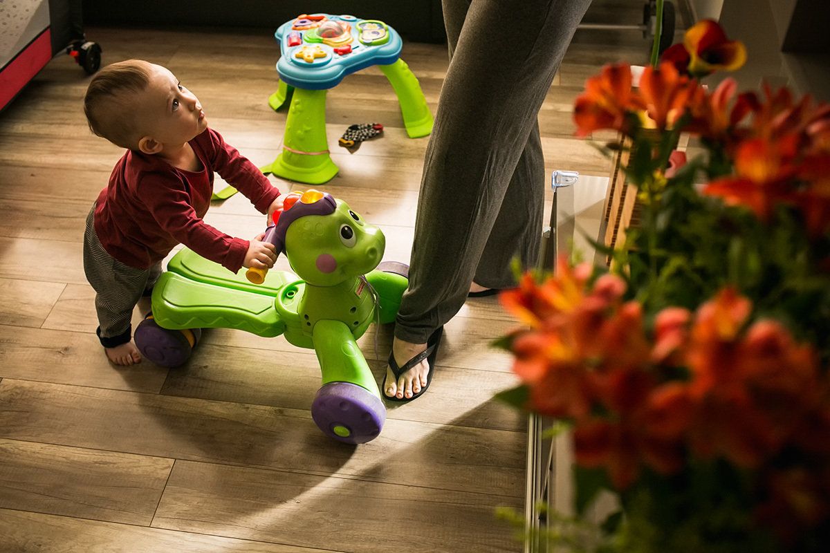bebê ficando em pé com a ajuda do brinquedo, sob supervisão da mãe em foto de Adriana Costa