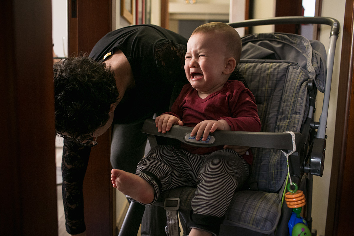 mãe colocando filho no carrinho e ele chorando