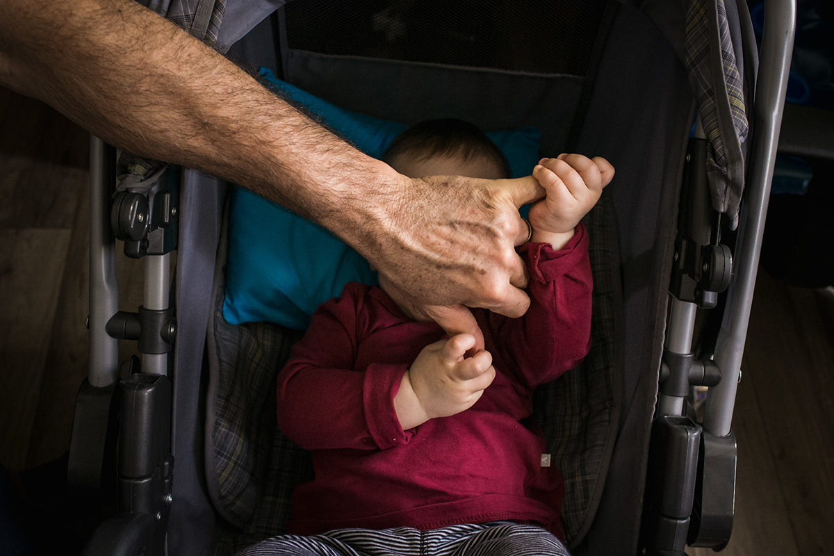 filho brincando com a mão do pai tentando dormir