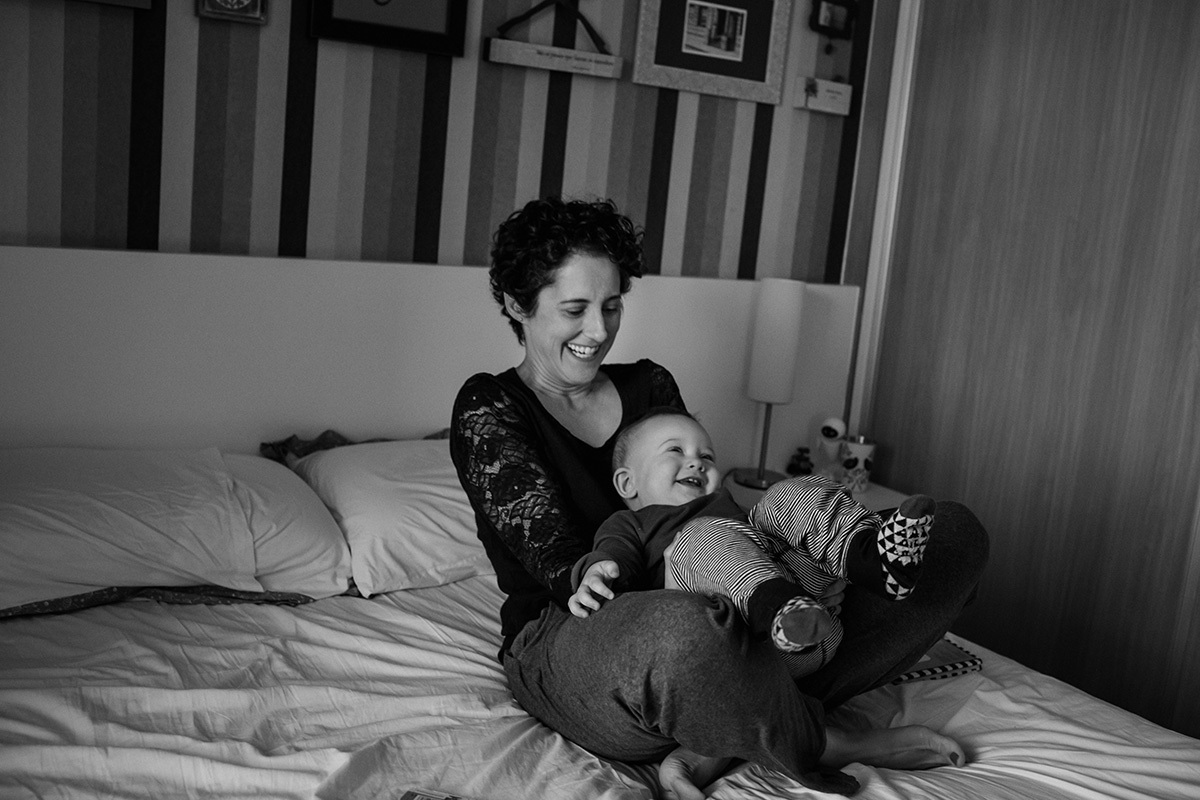 mãe brincando de balançar o seu bebê e sorrindo, por adrianacostafotos