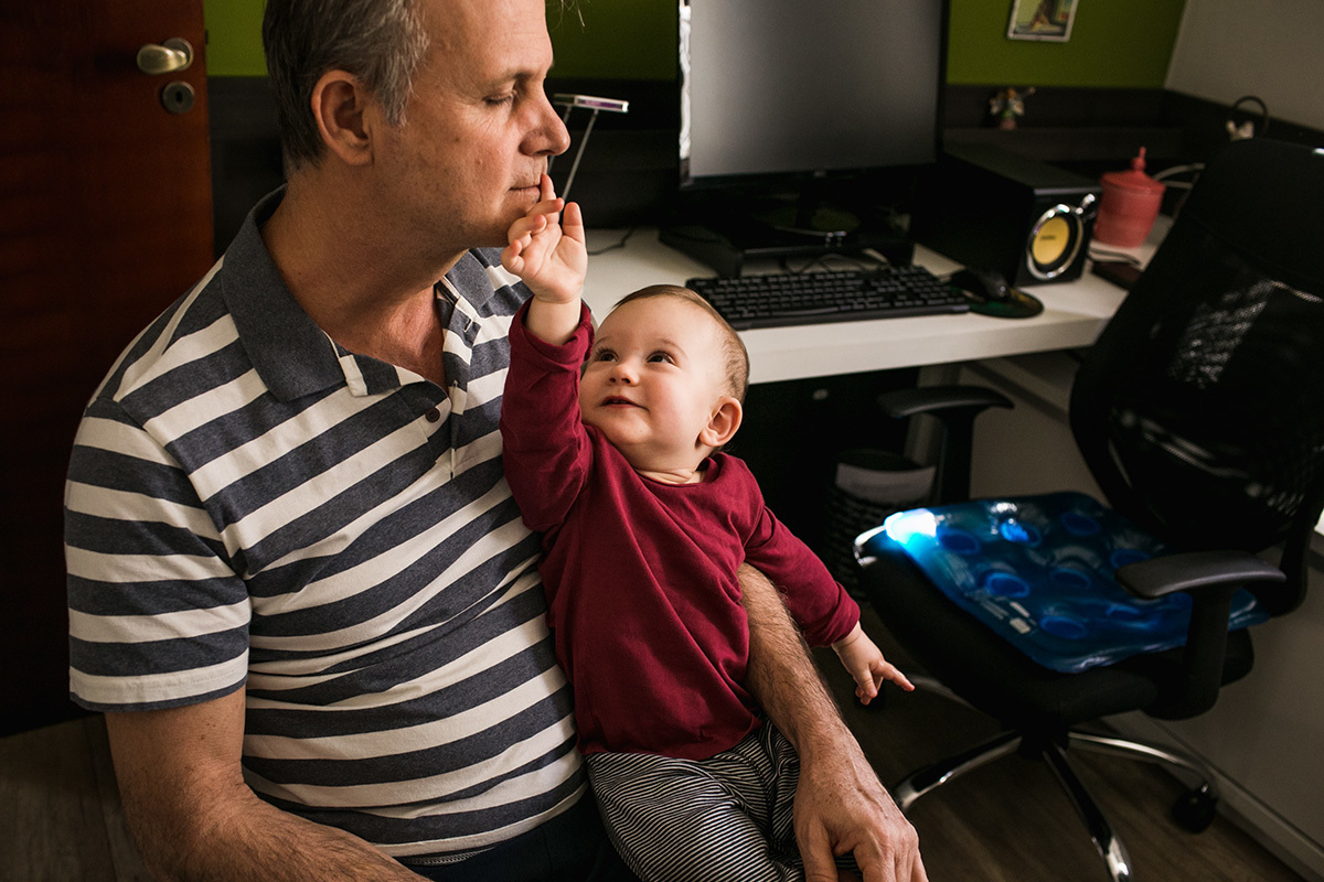 filho no colo do pai fazendo carinho em seu rosto, por Adriana Costa