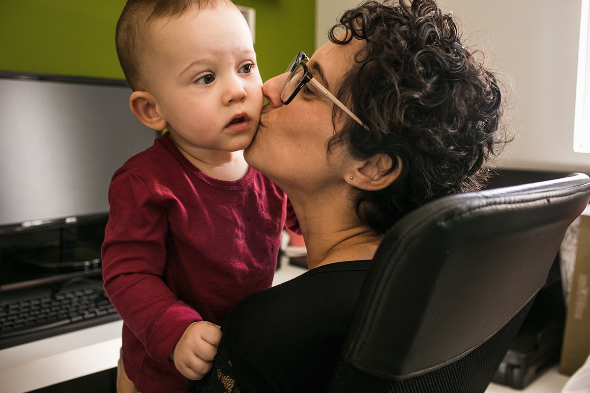 mãe beijando seu bebê que está em seu colo, por Adriana costa