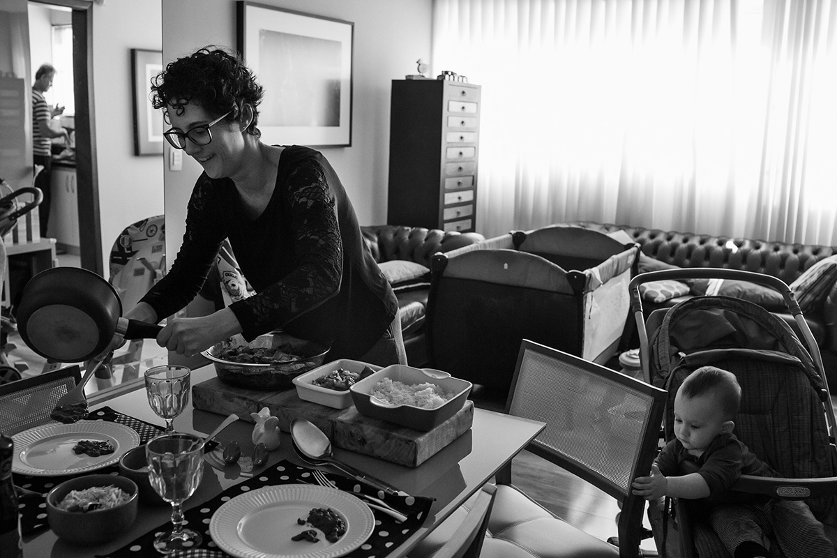 mãe servindo o almoço, pai na cozinha e bebê no carrinho em foto de Adriana Costa