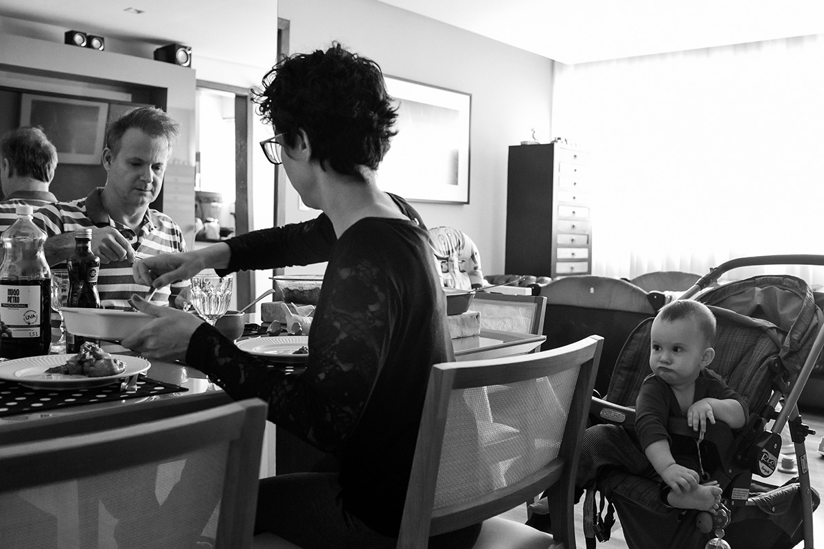 bebê fazendo careta enquanto seus pais almoçam na foto de Adriana Costa