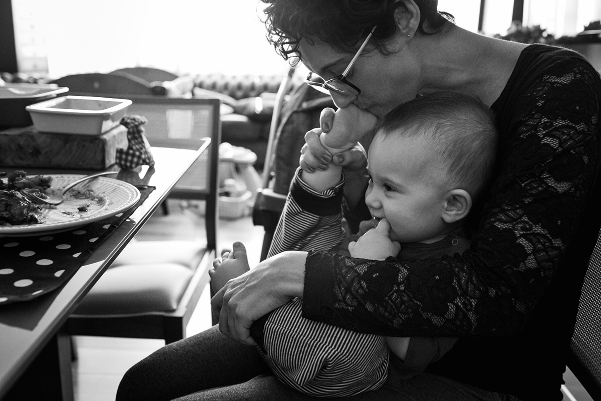 mãe almoçando e ao mesmo tempo brincando com seu bebê no colo, por Adriana Costa