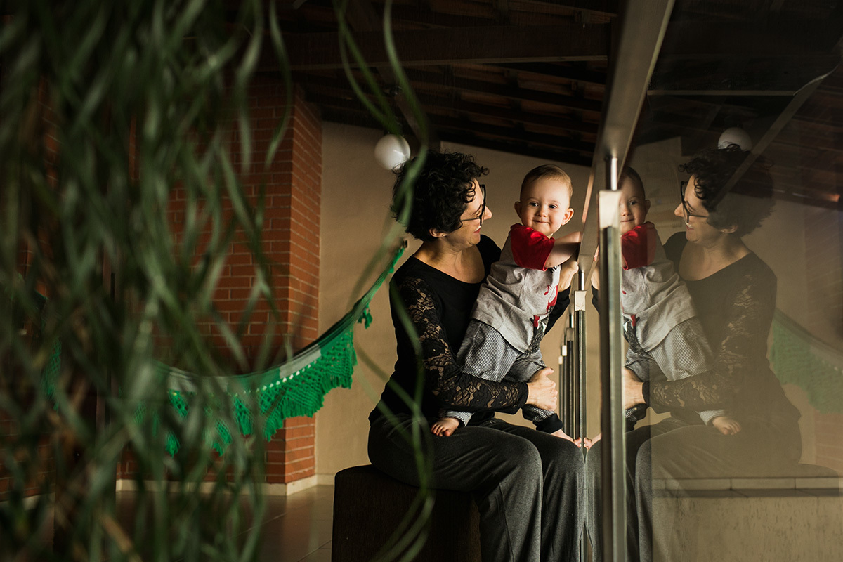 reflexo no vidro da mãe e filho brincando na varanda em foto de Adriana Costa