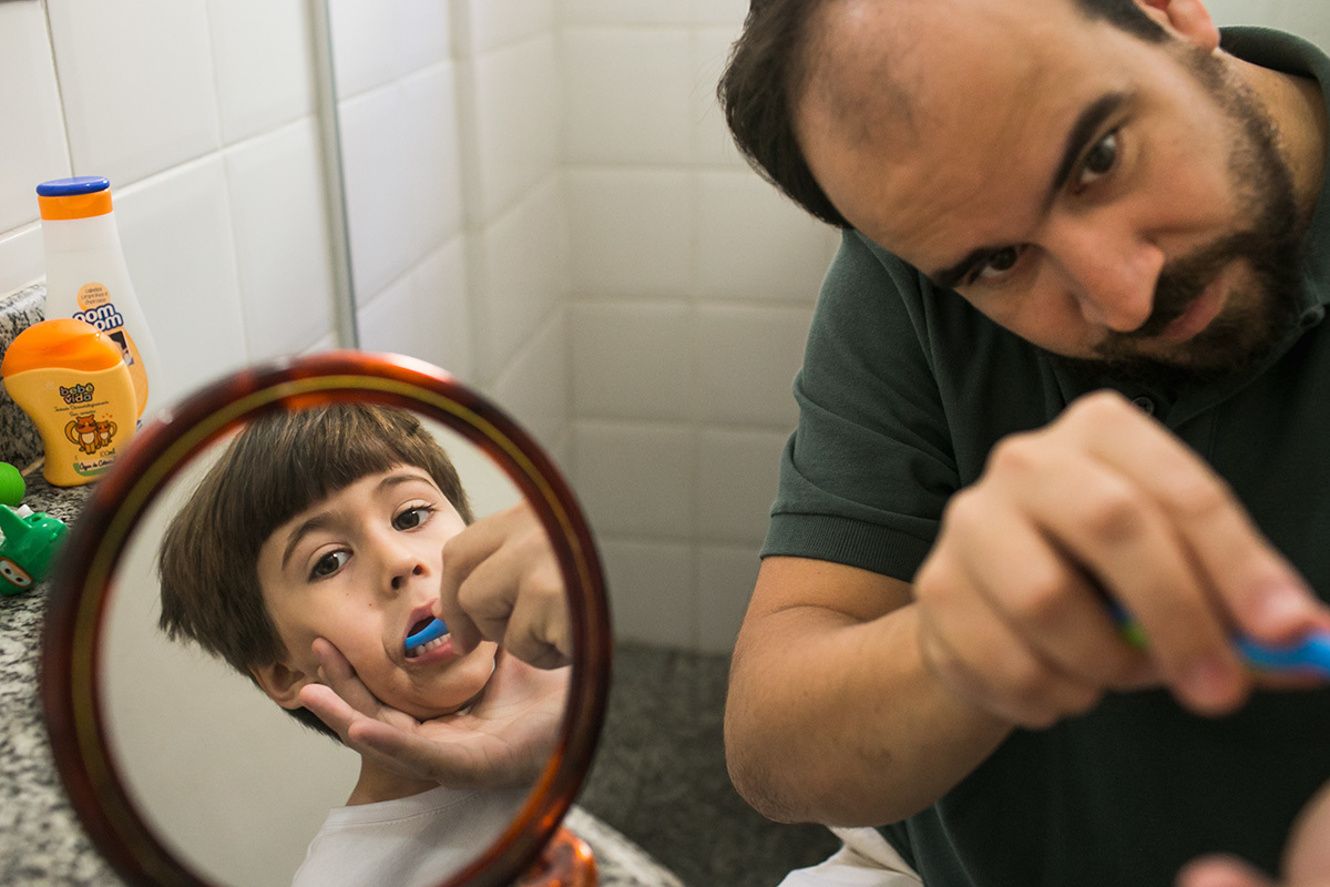 Adriana Costa fotografou o pai escovando os dentes do filho que aparece no reflexo do espelho