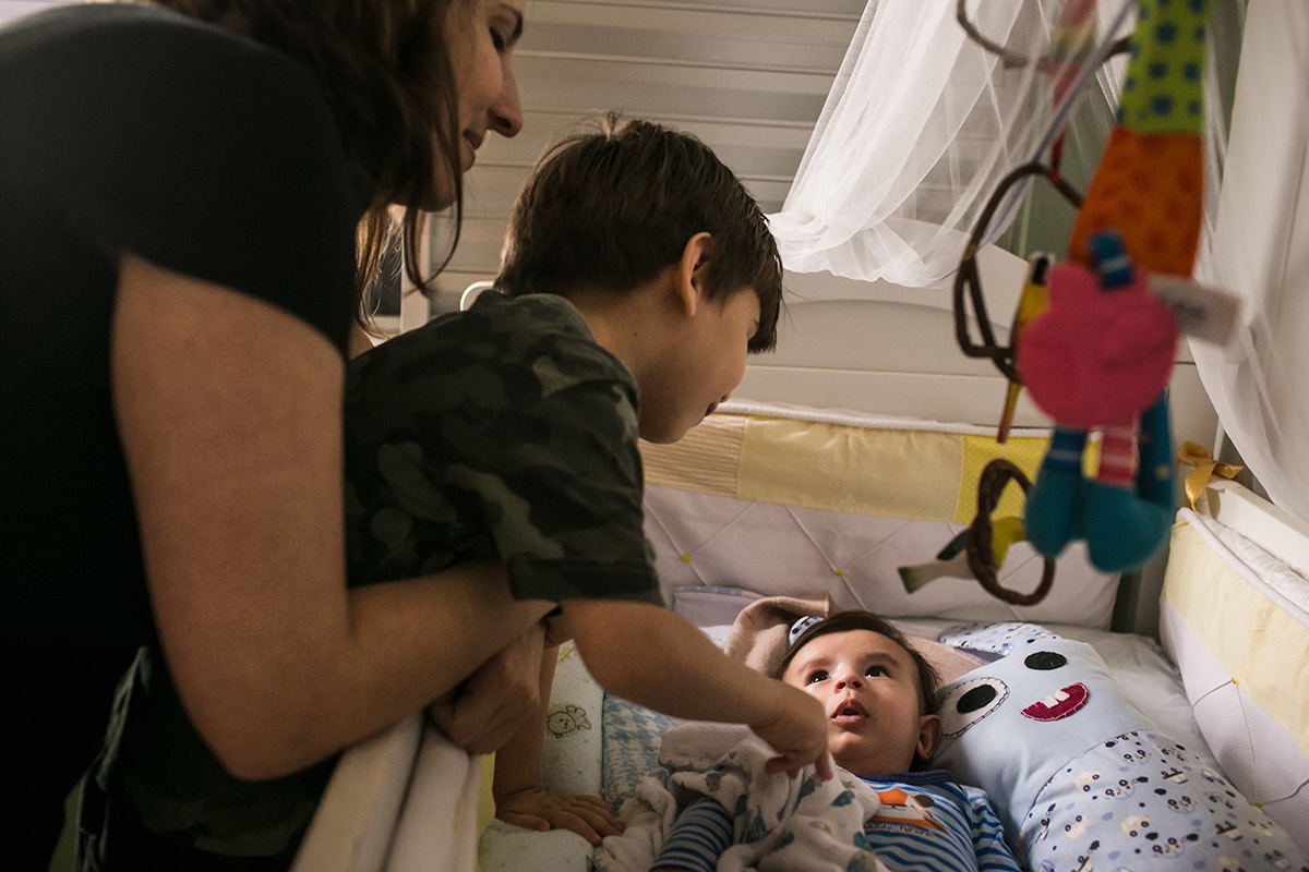 mãe e filho mais velho acordam o caçula da casa em um registro de Adriana Costa