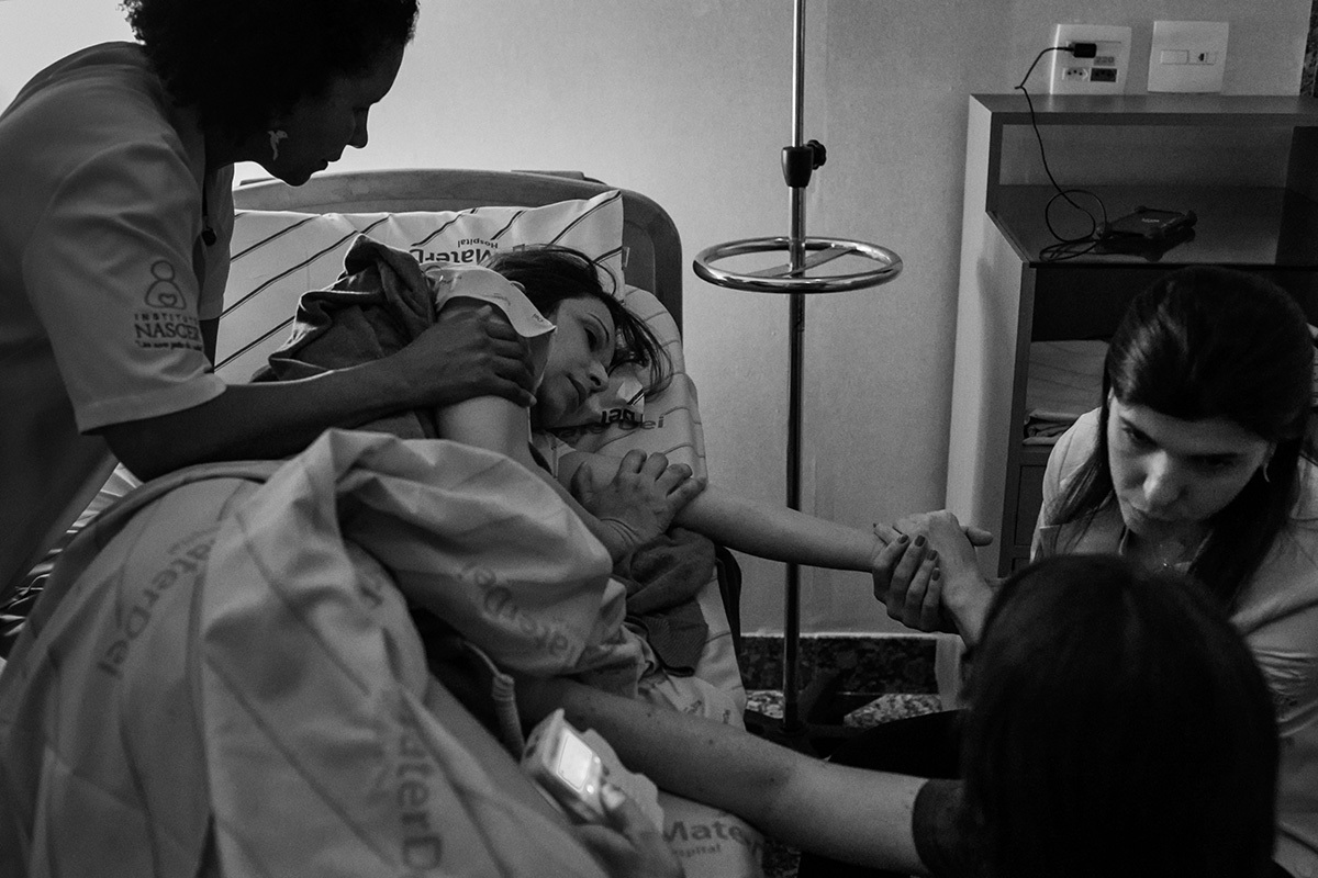 Foto de Adriana Costa da gestante recebendo o apoio da doula, enfermeira obstétrica e da médica obstetra durante o trabalho de parto