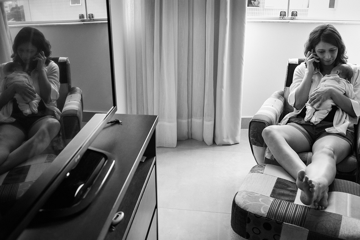 mãe conversando ao telefone com sua bebê dormindo no colo