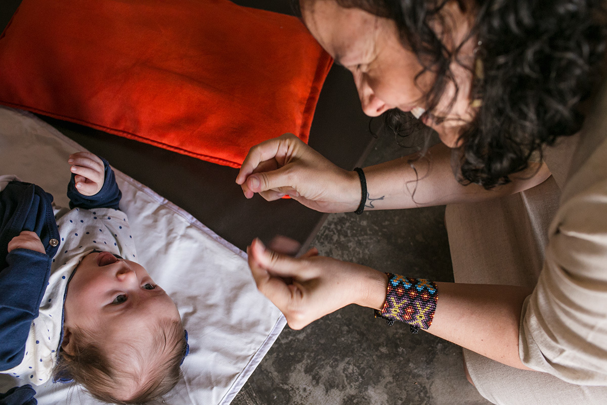 Foto de Adriana Costa da tia brincando e rindo com sua sobrinha enquanto ela troca a fralda