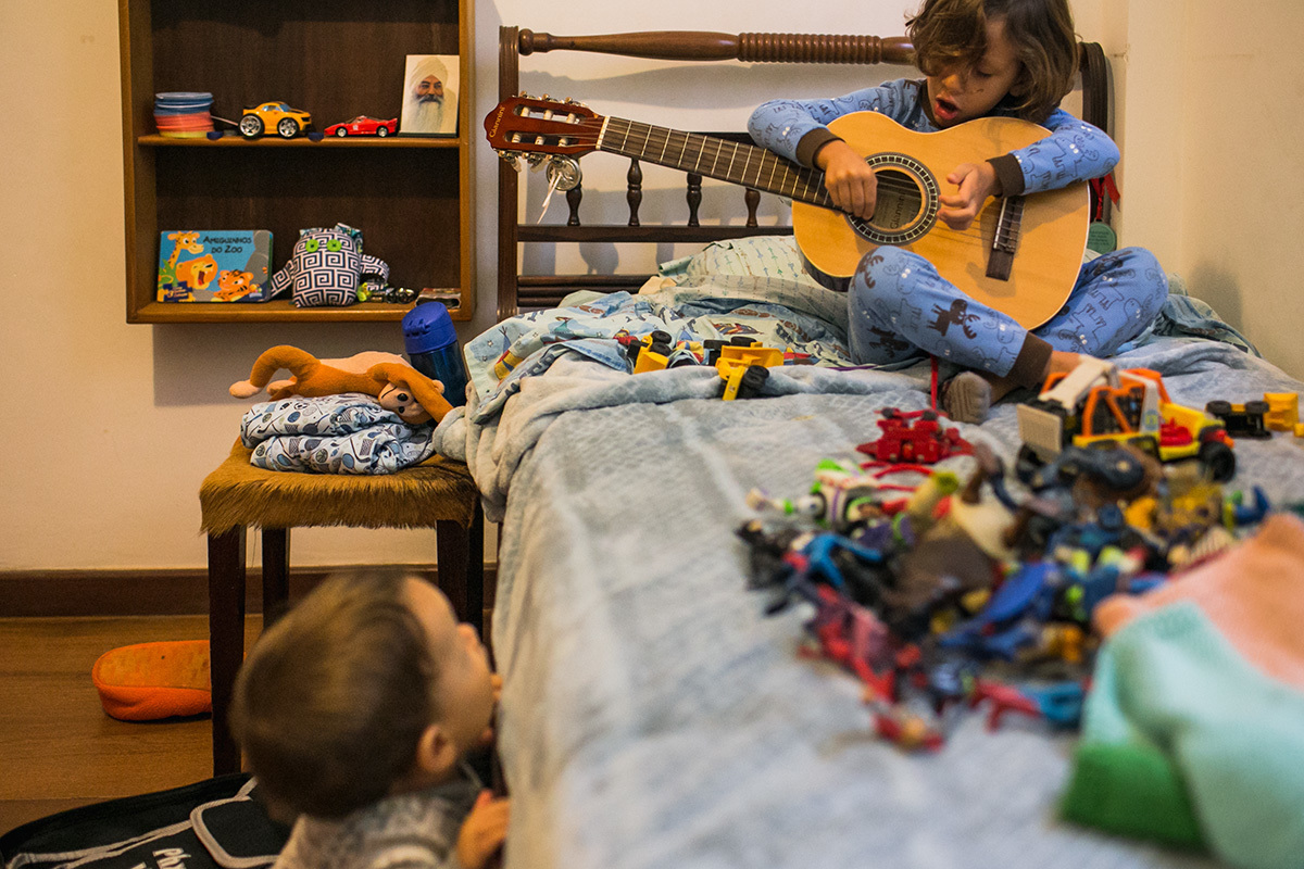 menino tocando violão e seu irmãozinho observando em foto de Adriana Costa