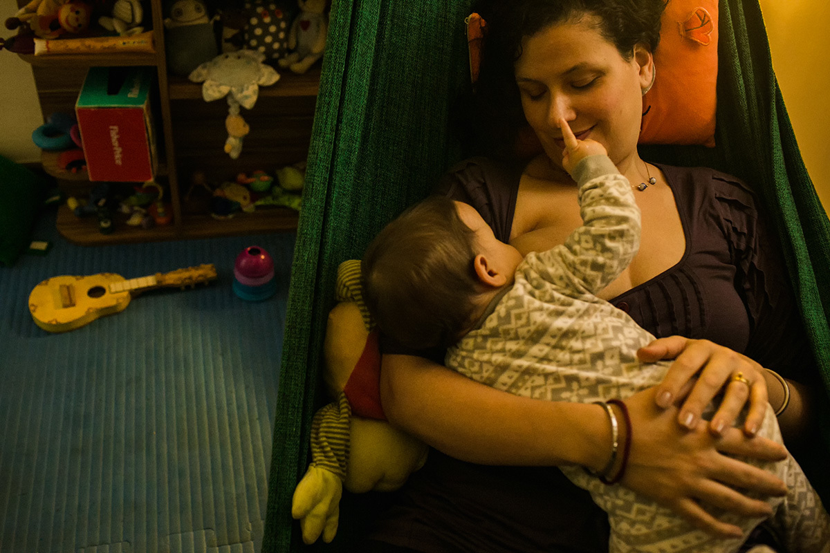 mãe fazendo seu bebê dormir amamentando numa rede de descanso, por Adriana Costa