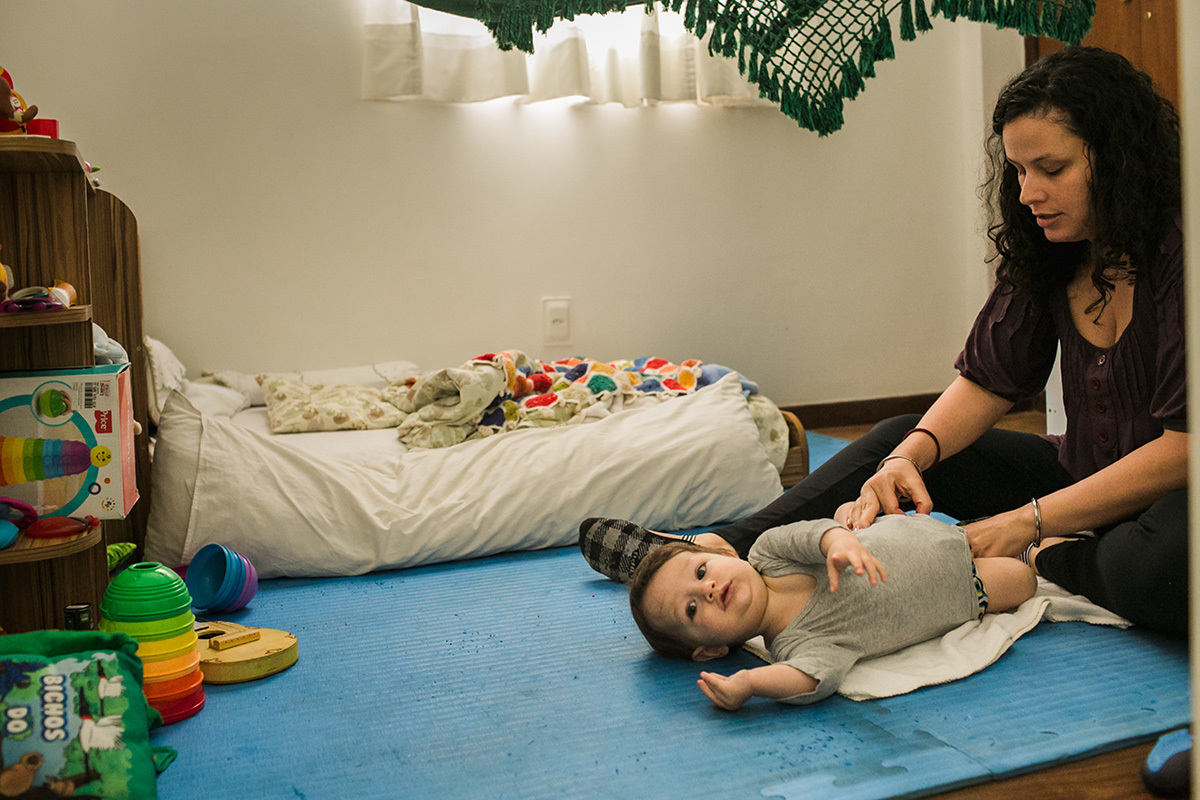 mãe tentando trocar a roupa do seu bebê que tenta fugir, em foto de Adriana Costa