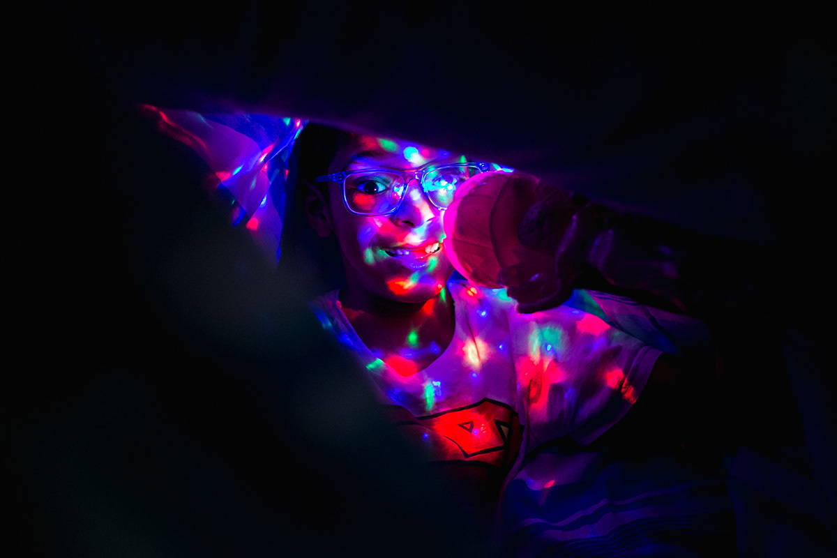 criança ilumina seu rosto no escuro com luzes coloridas, por adrianacostafotos