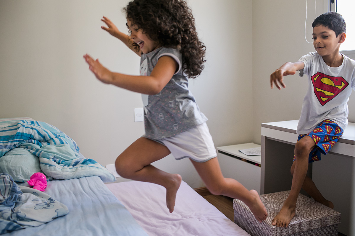 irmãos brincando de saltar do móvel para a cama, por Adriana Costa