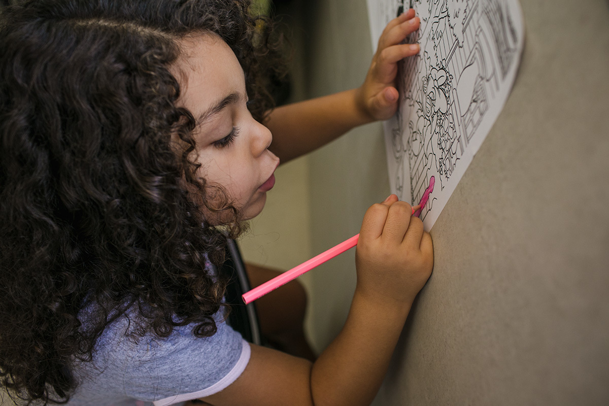 menina colorindo papel preso a parede, por Adriana Costa