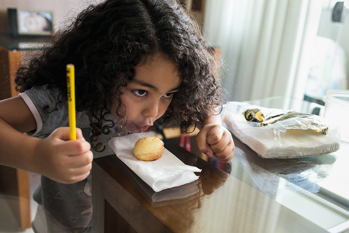 menina soprando pão de queijo para esfriar, por adrianacostafotos