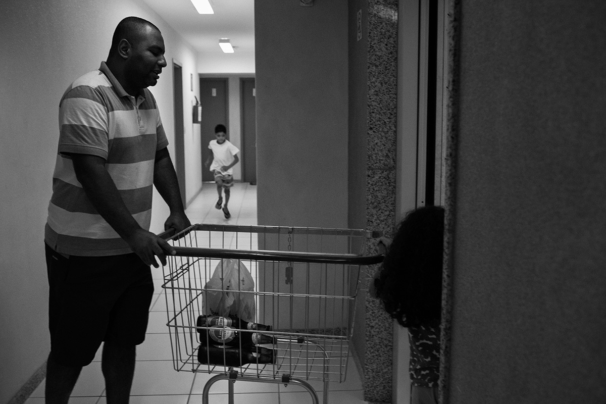 pai e crianças levando o carrinho de compras para o elevador