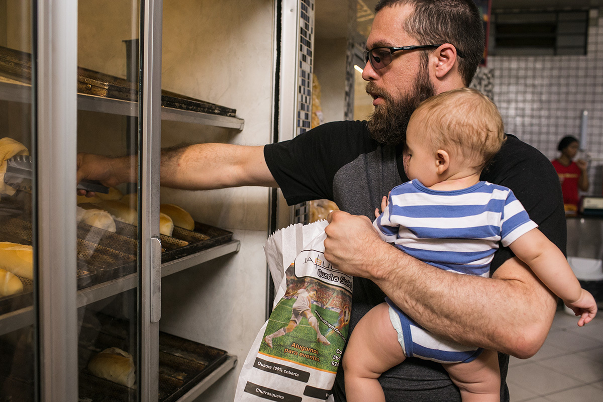 pai pegando pão na padaria com seu bebê no colo, em foto de Adriana costa