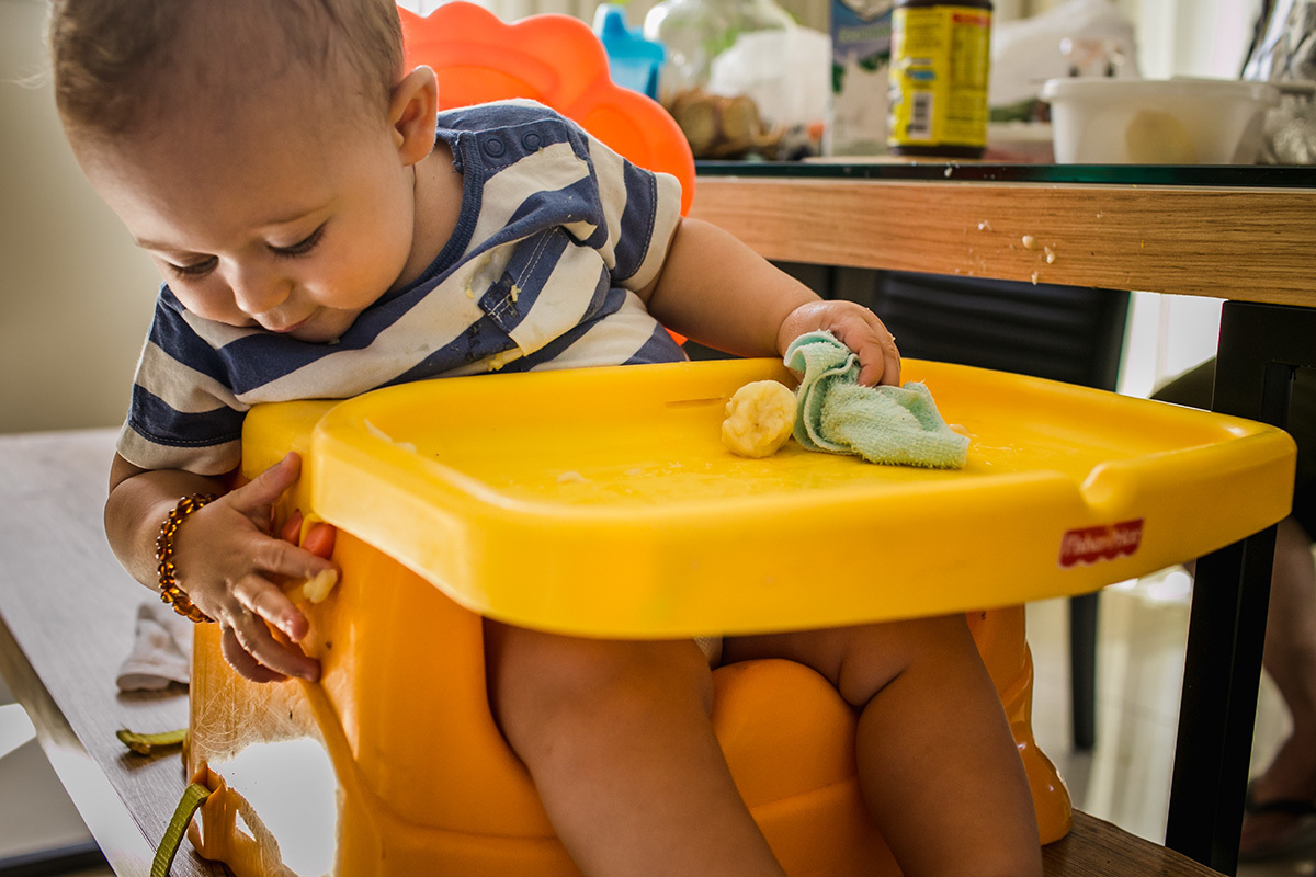 bebê passando a mão suja de banana na sua cadeirinha em foto de Adriana Costa